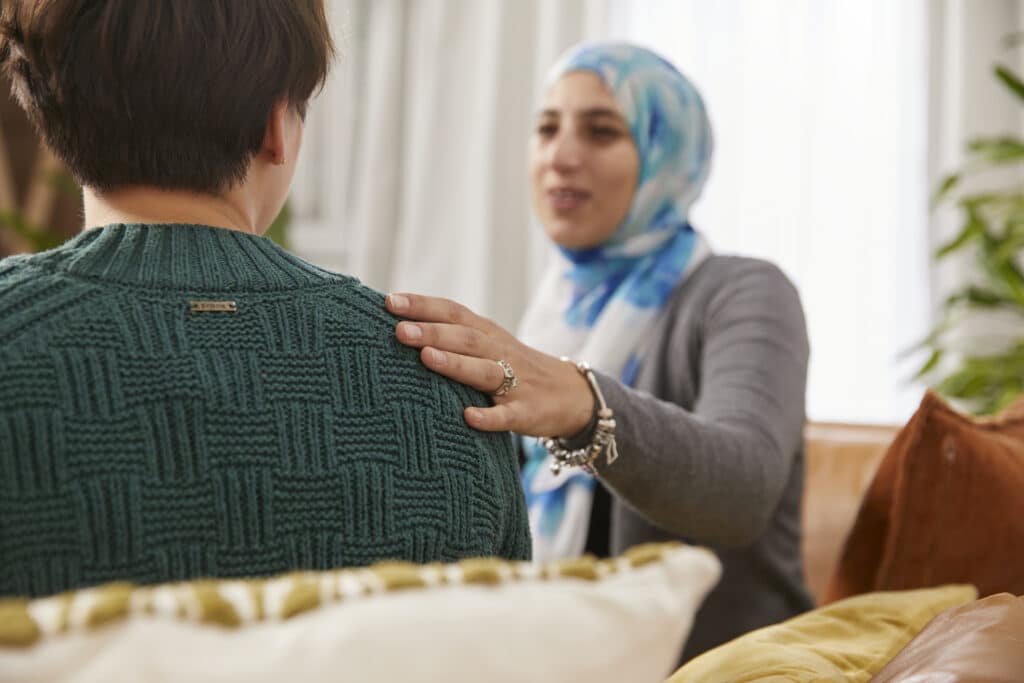 Health coach sitting with a patient with her hand on his shoulder providing comfort and support