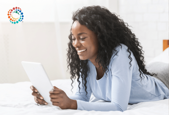 African amercian woman laying on her stomach looking at a tablet smiling and reading what is on the screen