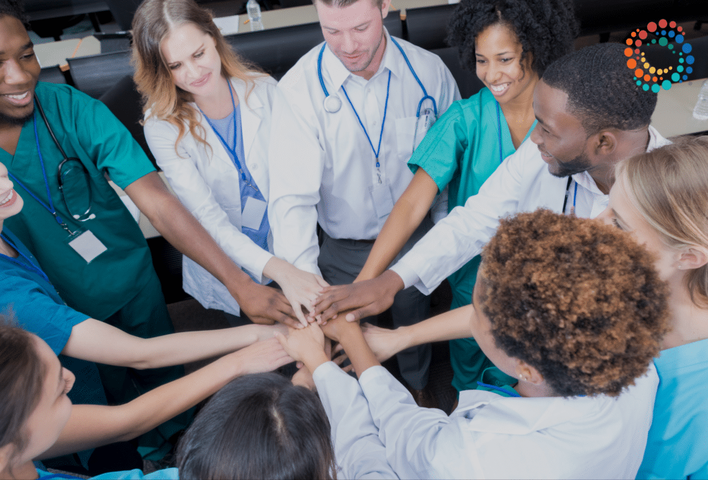 A group of diverse doctors with their hands in the middle of a circle to symbolize "in this together"