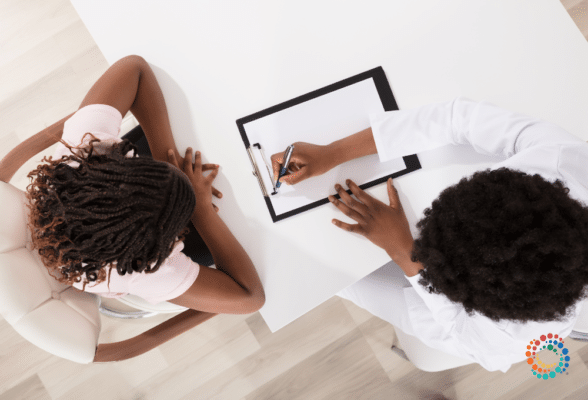 An african american doctor sitting with patient going over papers on a clip board used to portray a doctor taking the time to really learn and understand the patient