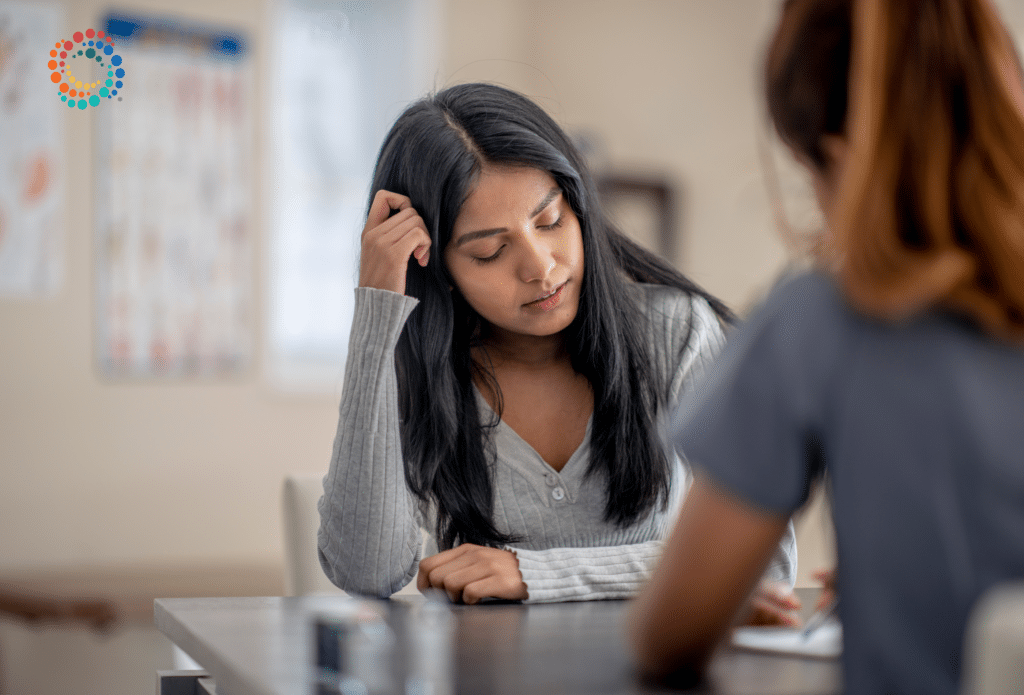 Woman with long black hair leaning her head on her hand looking down. Picture is used to depict "mental health" struggles